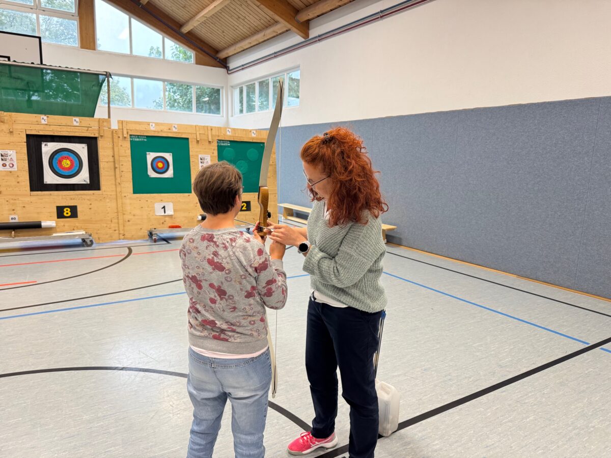 Bogenschiessen für Menschen mit Behinderung; Bogensportfreunde, Trainerin zeigt Frau wie ein Bogen gespannt wird